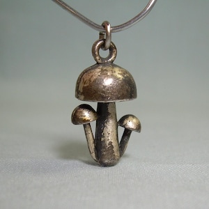 May include: Silver mushroom charm necklace featuring three mushrooms. The charm has a textured surface and a loop for attaching to a chain.