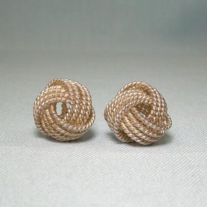 May include: A pair of gold-toned knot earrings. The earrings are made of a twisted rope design.