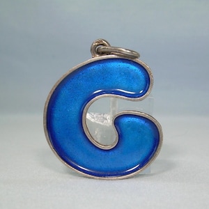 Peut inclure: Un pendentif de couleur argentée en forme de lettre majuscule G, doté d'une incrustation en émail bleu vif et brillant. Le pendentif comprend un petit anneau circulaire sur le dessus pour l'attache, avec un bord métallique lisse et poli.