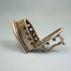 Op de afbeelding: Een zilverkleurige, scharnierende, decoratieve doos met een uitgesneden ontwerp. De doos is open en het deksel rust op de zijkant.