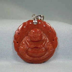 May include: A red carved jade pendant of a smiling Buddha, with a silver bail.