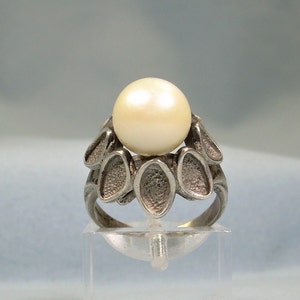 May include: A silver ring with a large, white pearl set in a cluster of leaf-shaped designs.