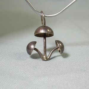 Puede incluir: Collar con colgante de plata con un diseño de hongo tridimensional con tres tapas de hongo.