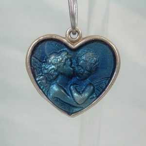 May include: A silver heart-shaped pendant with a blue enamel design of two angels kissing.