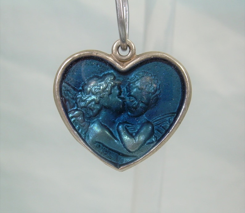 May include: A silver heart-shaped pendant with a blue enamel design of two angels kissing.