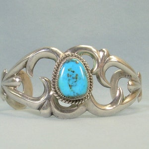 Op de afbeelding: Een zilveren armband met een turquoise steen in een decoratief ontwerp. De armband is gemaakt van sterling zilver en heeft een uniek, ingewikkeld ontwerp.