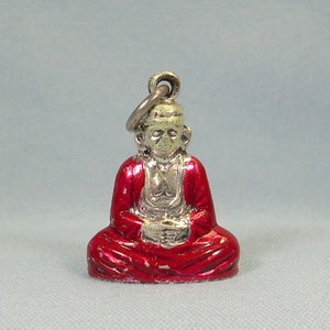 May include: A silver charm depicting a seated Buddha figure wearing a red robe. The charm has a loop at the top for attaching to a bracelet or necklace.