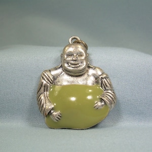 May include: Silver charm of a smiling Buddha holding a green jade-like stone. The charm is a pendant and has a loop at the top for attaching to a chain.