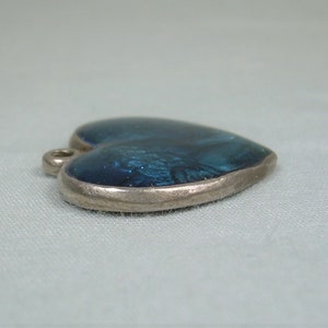 May include: A silver heart-shaped pendant with a blue enamel inlay. The enamel has a marbled effect.