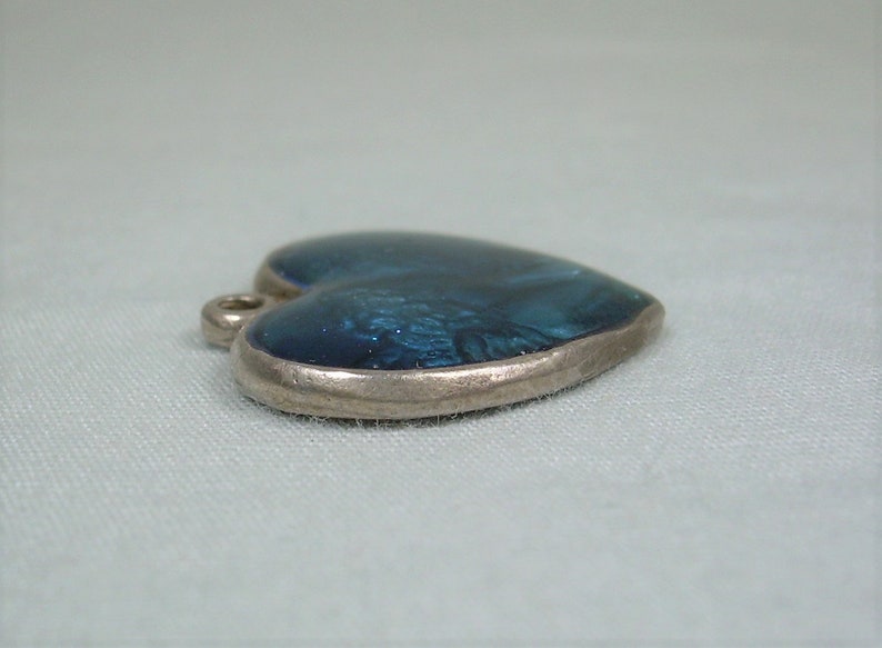 May include: A silver heart-shaped pendant with a blue enamel inlay. The enamel has a marbled effect.