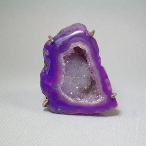 以下が含まれることがあります： 金色の枠にセットされた紫色のジオードのリング。ジオードは内部に自然な結晶の形成があります。