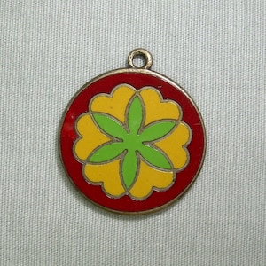 Puede incluir: Un colgante redondo de metal rojo con un diseño de flor amarilla y verde. La flor tiene cinco pétalos y un centro verde.