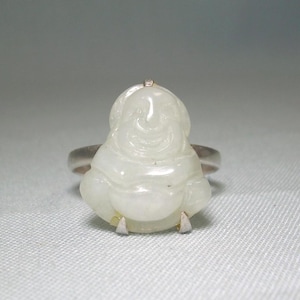 May include: A white jade ring featuring a carved depiction of a smiling Buddha. The ring is set in silver.