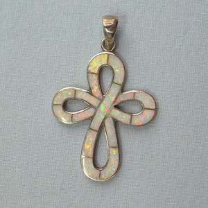 May include: A silver pendant in the shape of a cross with an infinity loop design. The cross is inlaid with iridescent white opal stones. The pendant has a silver bail for attaching to a chain.