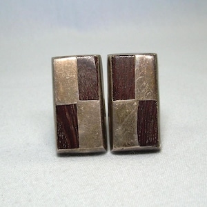 May include: A pair of silver cufflinks with a checkered pattern of dark wood and silver.