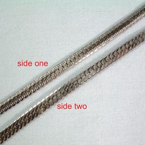 Puede incluir: Una cadena de collar de espiga en tono plateado mostrada desde dos ángulos diferentes. La hebra superior está etiquetada como side one y presenta un patrón tejido texturizado. La hebra inferior está etiquetada como side two y es plana.