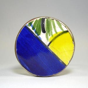 May include: A round ceramic knob with a blue, yellow, green, and white geometric design.