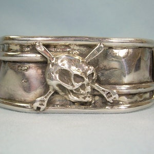 May include: A silver bracelet shaped like a drum with a skull and crossbones design.