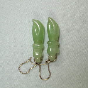 May include: A pair of green jade earrings with a carved design. The earrings are suspended from gold-toned hooks.