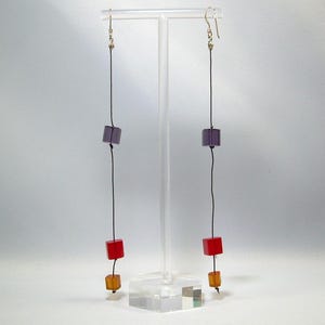 May include: A pair of long dangle earrings with black string and three colored beads. The top bead is purple, the middle bead is red, and the bottom bead is amber.