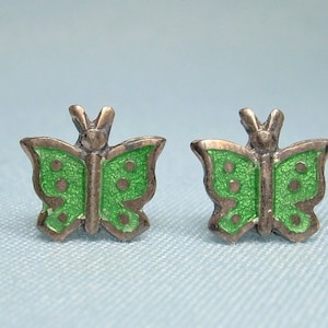 May include: A pair of silver butterfly earrings with green enamel. The butterflies have a detailed design with spots on their wings.