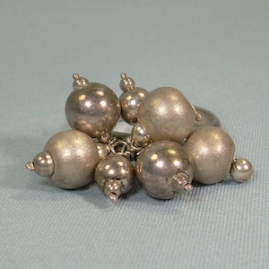 May include: A silver ring with multiple round beads attached. The beads are clustered together and appear to be made of a smooth, metallic material.