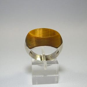 May include: A silver ring with a large, oval-shaped tiger's eye gemstone. The ring is set in a simple band.