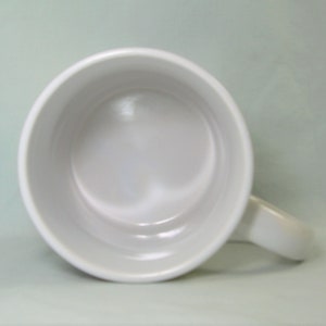 May include: White ceramic mug with a rounded handle. The mug is empty and the inside is visible.
