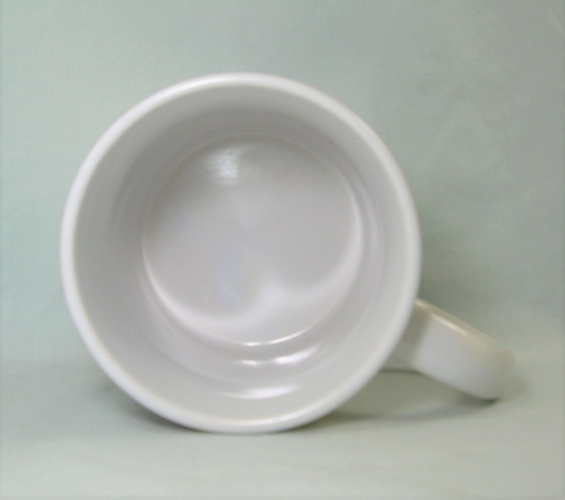 May include: White ceramic mug with a rounded handle. The mug is empty and the inside is visible.