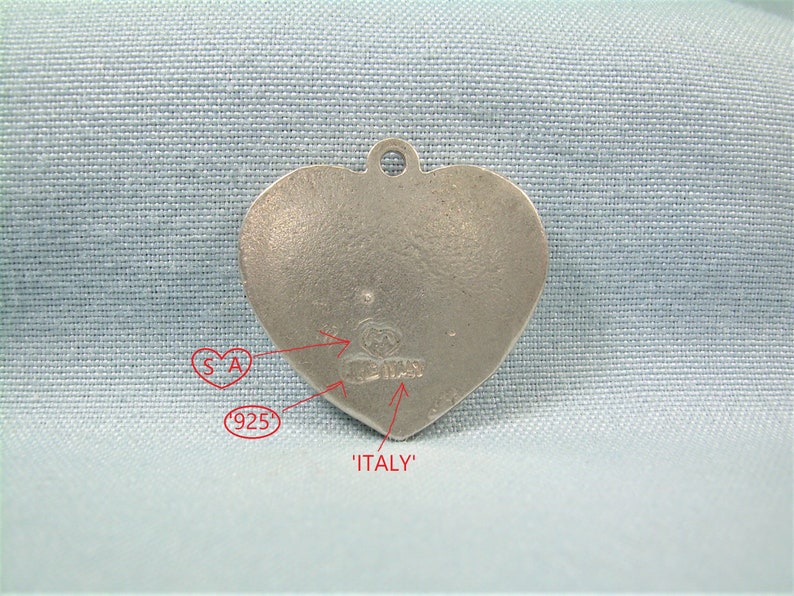 May include: Silver heart-shaped charm with the words 'ITALY' and '925' stamped on the back. The charm also has the letters 'SA' and a maker's mark.
