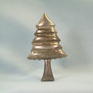 May include: A silver-toned metal Christmas tree ornament in the shape of a stylized pine tree. The ornament has a textured surface and a simple, elegant design.