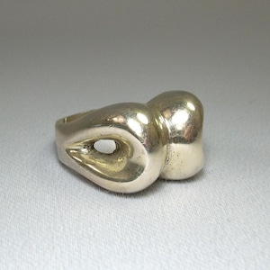 May include: A silver ring with an abstract design. The ring features a teardrop-shaped element with an oval opening, connected to a rounded, bulbous shape. The ring is set against a neutral background, highlighting its unique form.