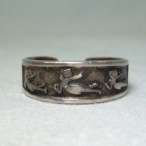 May include: A silver ring with a band featuring a repeating design of stylized figures. The figures are in a running pose and appear to be wearing hats.