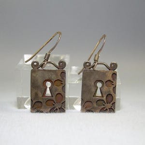 May include: A pair of silver earrings with a keyhole design and floral accents. The earrings are made of metal and have a silver finish.