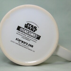 May include: White ceramic mug with a black Star Wars logo and Galerie branding. The mug is dishwasher and microwave safe. The bottom of the mug has the text "starwars.com" and a phone number.