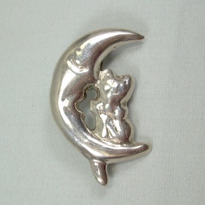May include: A silver crescent moon brooch with a small bear cub sitting inside the curve of the moon.