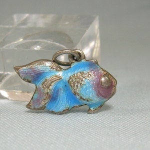May include: A silver charm in the shape of a blue and purple fish with a silver eye. The charm is enameled and has a detailed design.
