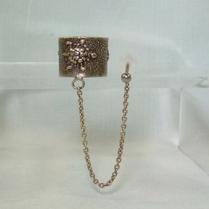 May include: Silver ear cuff with a chain connecting to a silver stud earring. The cuff has a textured design and the stud has a small ball on the end.