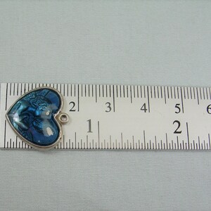 May include: A blue and silver heart-shaped charm with a detailed image of a couple embracing. The charm is approximately 1 inch in size and has a loop for attaching to a necklace or bracelet.