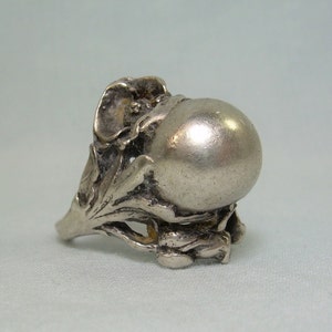 Op de afbeelding: Een zilveren ring met een grote, ronde, gladde, bolvormige middelste steen. De band is ingewikkeld ontworpen met een bloemmotief.