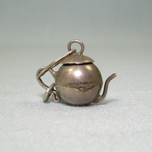 Puede incluir: Un charm de plata con forma de tetera con tapa. El charm tiene un bucle en la parte superior para sujetarlo a una pulsera o collar.