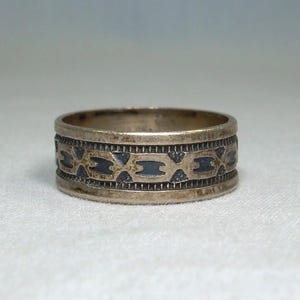 May include: A silver ring with a detailed band featuring a repeating geometric pattern with dark blue accents. The ring has a slightly worn appearance, suggesting it is vintage or antique.