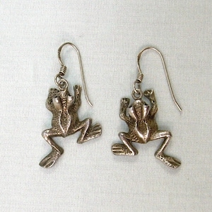 Peut inclure: Une paire de boucles d'oreilles pendantes en argent en forme de grenouille. Les grenouilles sont détaillées et ont une finition texturée.