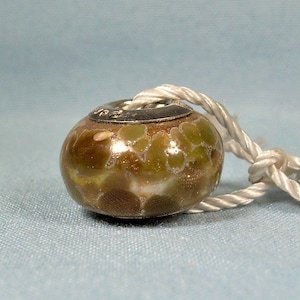 May include: A brown and green glass bead with a silver charm. The bead has a speckled pattern and is attached to a white cord.