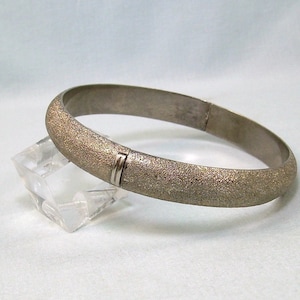May include: A silver bangle bracelet with a textured finish. The bracelet has a hinged clasp.