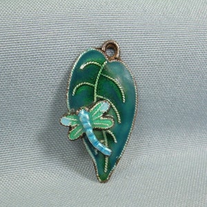 May include: A green enamel pendant shaped like a leaf with a blue and green dragonfly on it.