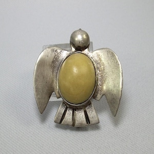 Op de afbeelding: Een zilveren vogel broche met een gele steen in het midden. De vogel heeft uitgespreide vleugels en een gedetailleerd ontwerp.