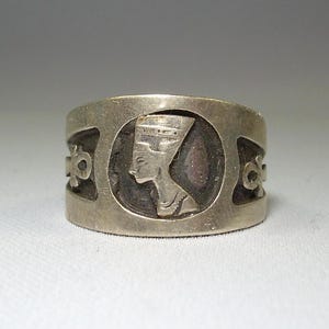May include: Silver ring with a profile of an Egyptian queen wearing a crown and a detailed design around the band.