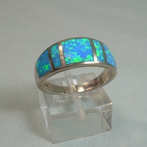 Puede incluir: Un anillo de banda de plata con incrustaciones de ópalo azul y verde. El anillo tiene cinco piedras de ópalo rectangulares engastadas en una banda de plata.