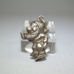 May include: Silver charm of a cartoon character wearing a hat and coat, standing on ice skates.